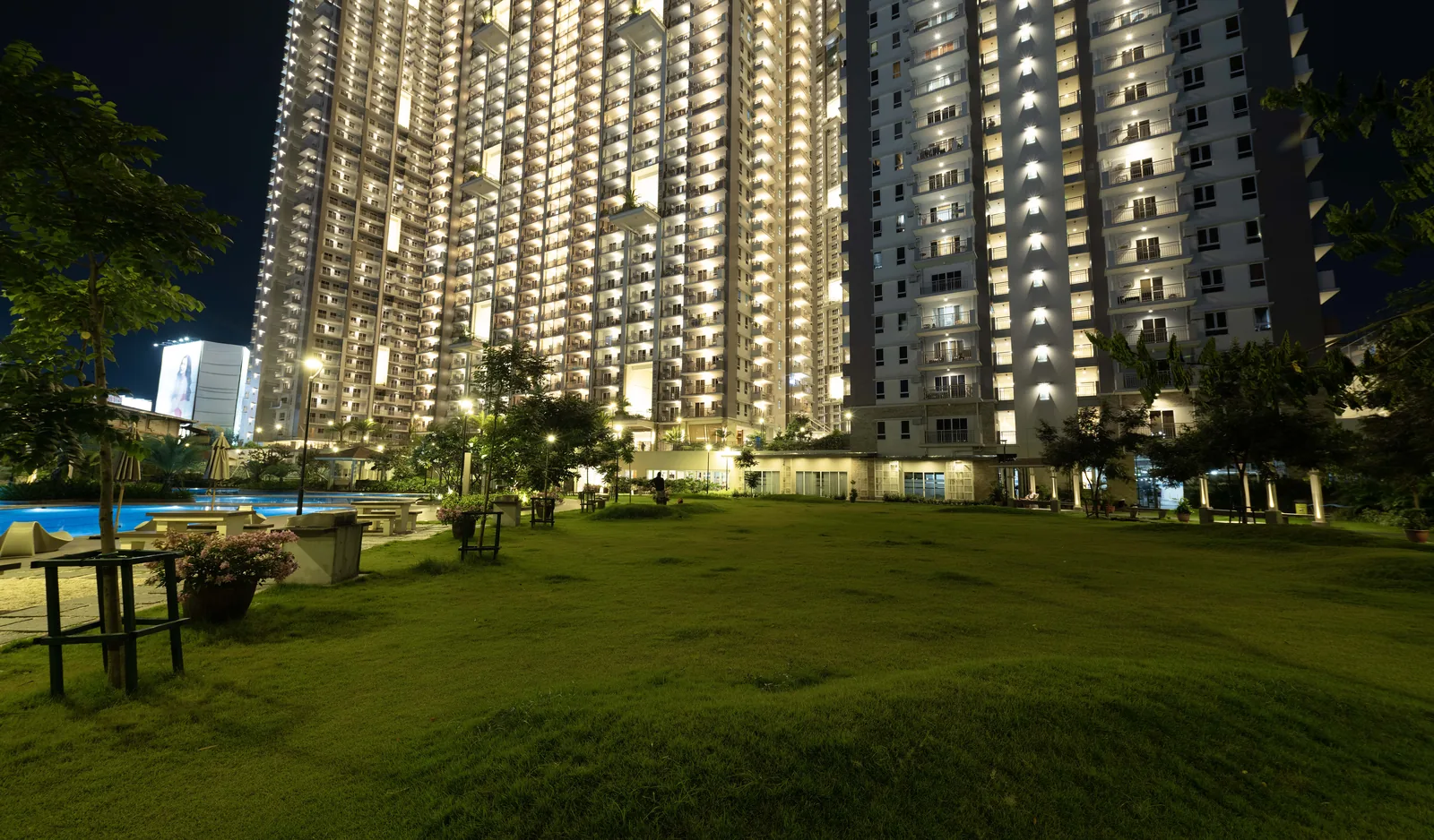The open lawn at Prisma Residences at night, towers lit behind